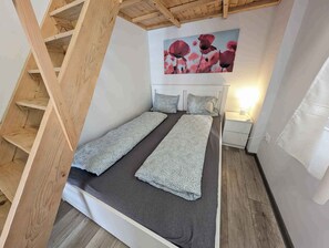 A bedroom with a bed, a nightstand, a lamp, a wooden staircase, and a painting of flowers. - Holiday home with Wi-Fi and air conditioning (Siófok)