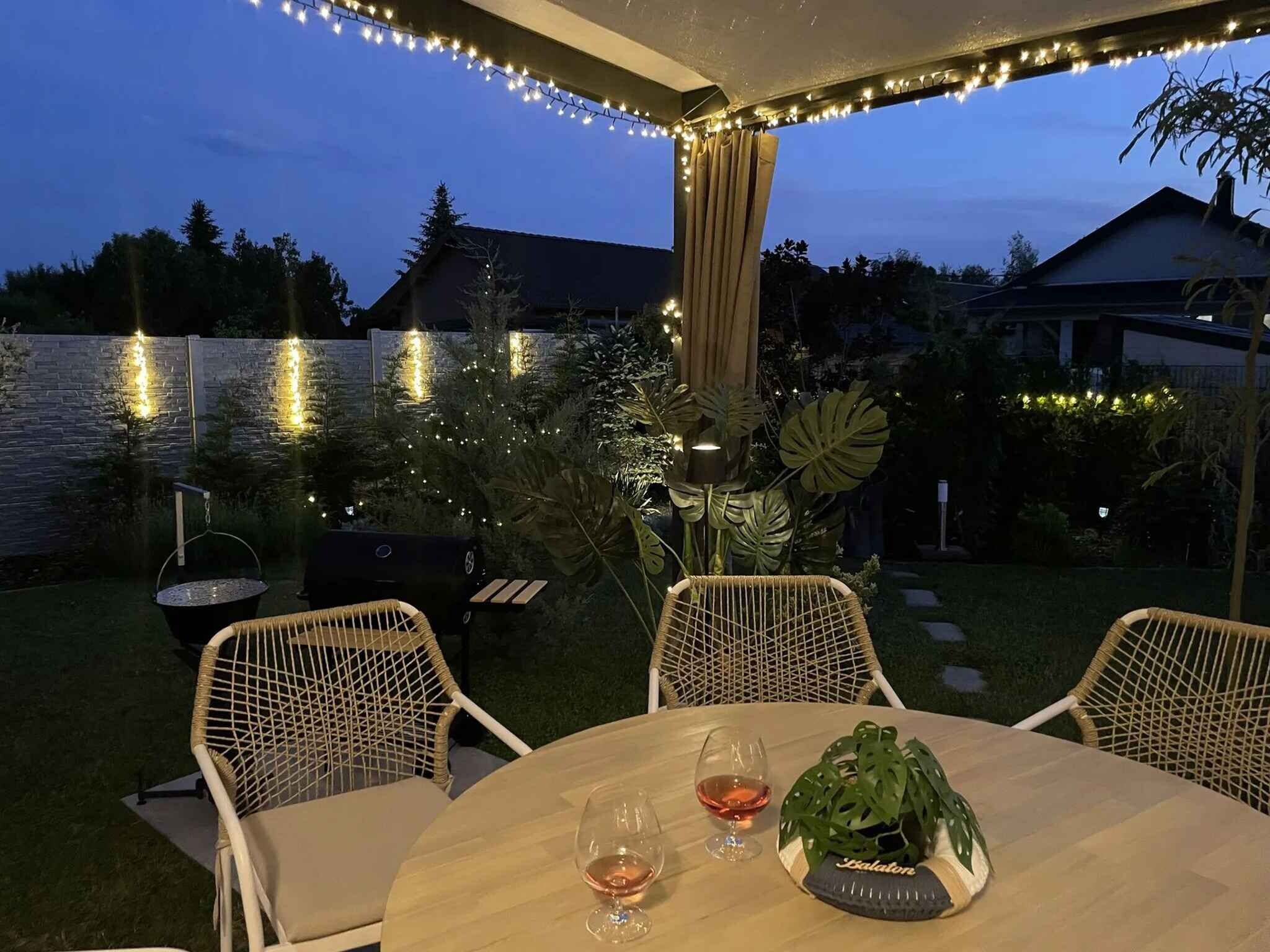 An outdoor patio with a table and chairs, string lights, and a grill.