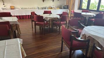 Un espace repas comprenant plusieurs tables et chaises, un plancher en bois et une vue dégagée grâce à de grandes fenêtres.