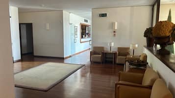 Un vestíbulo de hotel con piso de madera, un mostrador de recepción, una zona de estar y una planta en el mostrador.