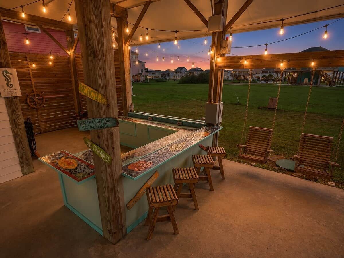 A covered outdoor bar area with a mosaic bar top, wooden stools, and string lights.
