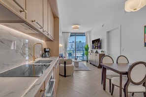A modern kitchen with a marble countertop, a built-in stove, and a dining area with a table and chairs. - Luxe NoMad Wynwood 1BR Balcony & Rooftop (Miami)