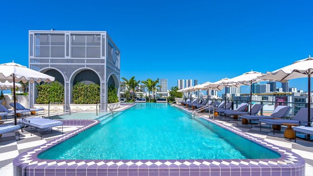 A swimming pool with lounge chairs and umbrellas, surrounded by a modern building with arched windows. - Luxe Wynwood 1BR · Balcony + Rooftop Pool, Miami (Miami)