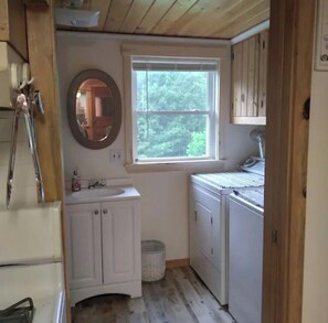 A compact kitchen with white cabinets, a window, and a mirror. - Comfortable family retreat tucked away in the western mountains of Maine. (Weld)