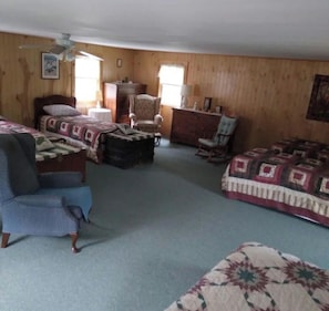 Ein Zimmer mit einem Bett, zwei Sesseln, einer Holzkommode und einem Deckenventilator.