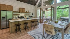 Una cocina con isla central, taburetes de bar y comedor con mesa dispuesta para cuatro.