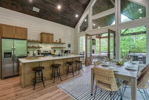 A kitchen with a central island, bar stools, and a dining area with a table set for four. - New! Twisted Wildflower! Spa, Fire-pit, Foosball! (Broken Bow)