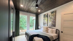 Un dormitorio con una cama, ventilador de techo, un cuadro y vistas al exterior.