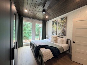 A bedroom with a bed, a ceiling fan, a painting, and a view of the outdoors. - New! Twisted Wildflower! Spa, Fire-pit, Foosball! (Broken Bow)