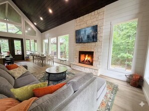 A living room with a stone fireplace, a large TV mounted on the wall, and a cozy seating area. - New! Twisted Wildflower! Spa, Fire-pit, Foosball! (Broken Bow)