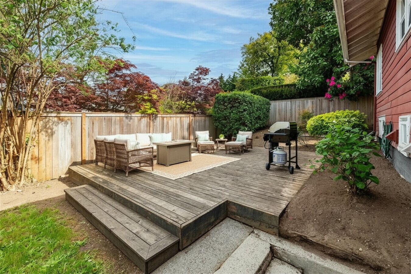 A backyard deck with outdoor furniture, a grill, and a wooden fence.