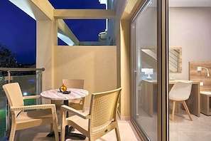 A balcony with wicker chairs, a small round table, and a glass door leading to an indoor area with a desk and chair. - Grape Vine (Zakynthos)