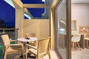 A balcony with wicker chairs, a small round table, and a glass door leading to an indoor area with a desk and chair.