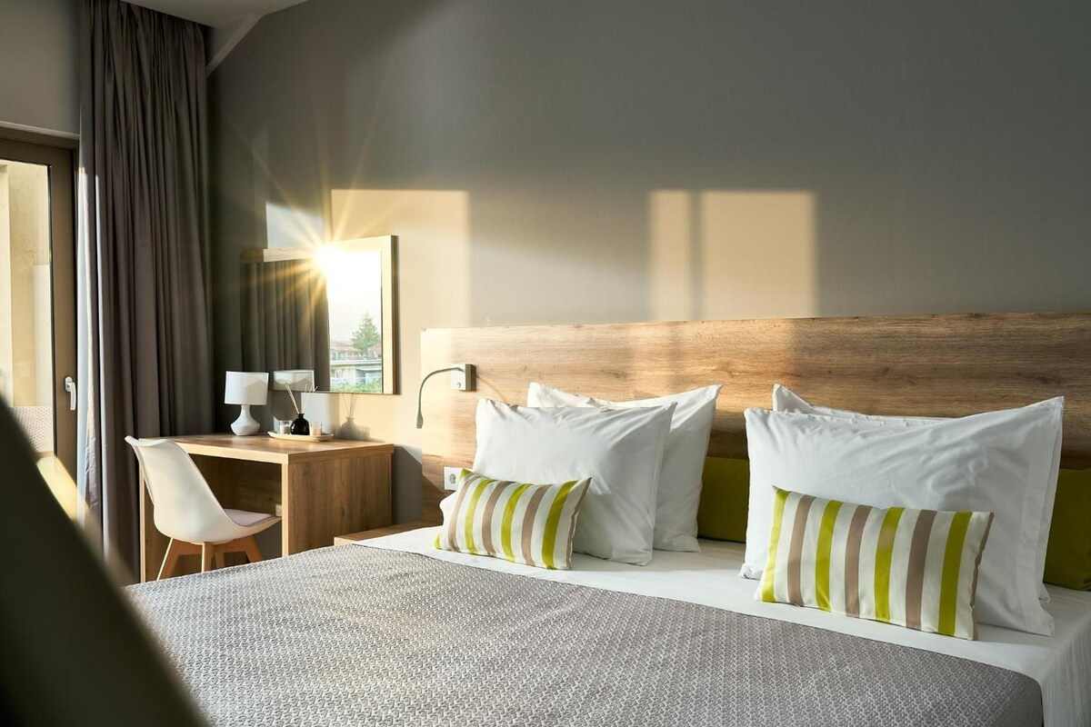 A hotel room with a large bed, a desk, a chair, and a window with curtains.