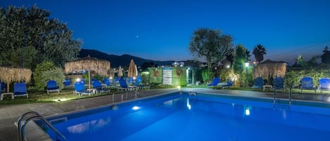 Una piscina con sillas de descanso y un flotador salvavidas, rodeada de árboles y una montaña al fondo.