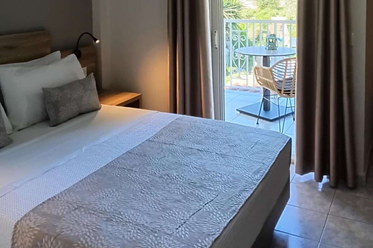 Un dormitorio con cama, mesita de noche, ventana con cortinas y vista a un patio exterior.
