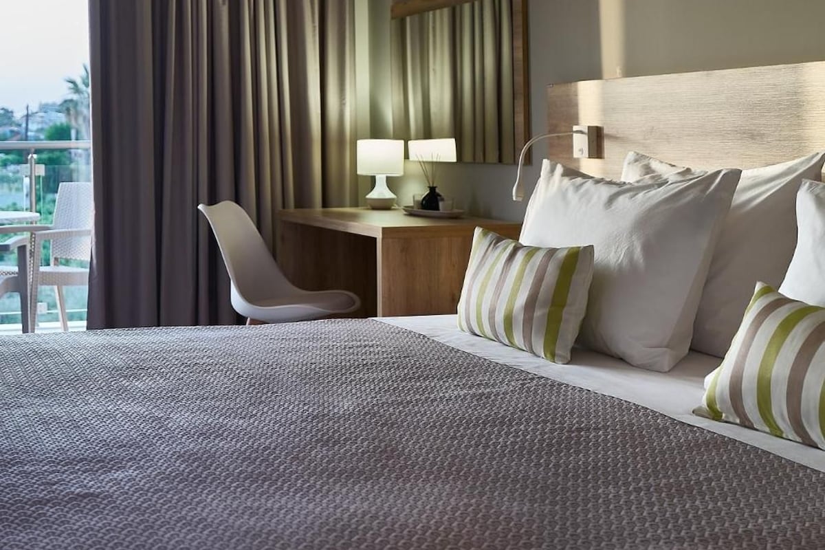 A hotel room with a large bed, a desk with a lamp, a chair, and a view of the outdoors.
