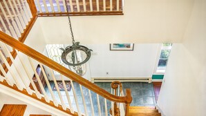 A wooden staircase with white railings, a hanging light fixture, and a view of a room with a tiled floor and a window.