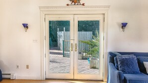 A room with a sliding glass door leading to a wooden deck, a blue sofa with patterned cushions, and wall-mounted sconces.