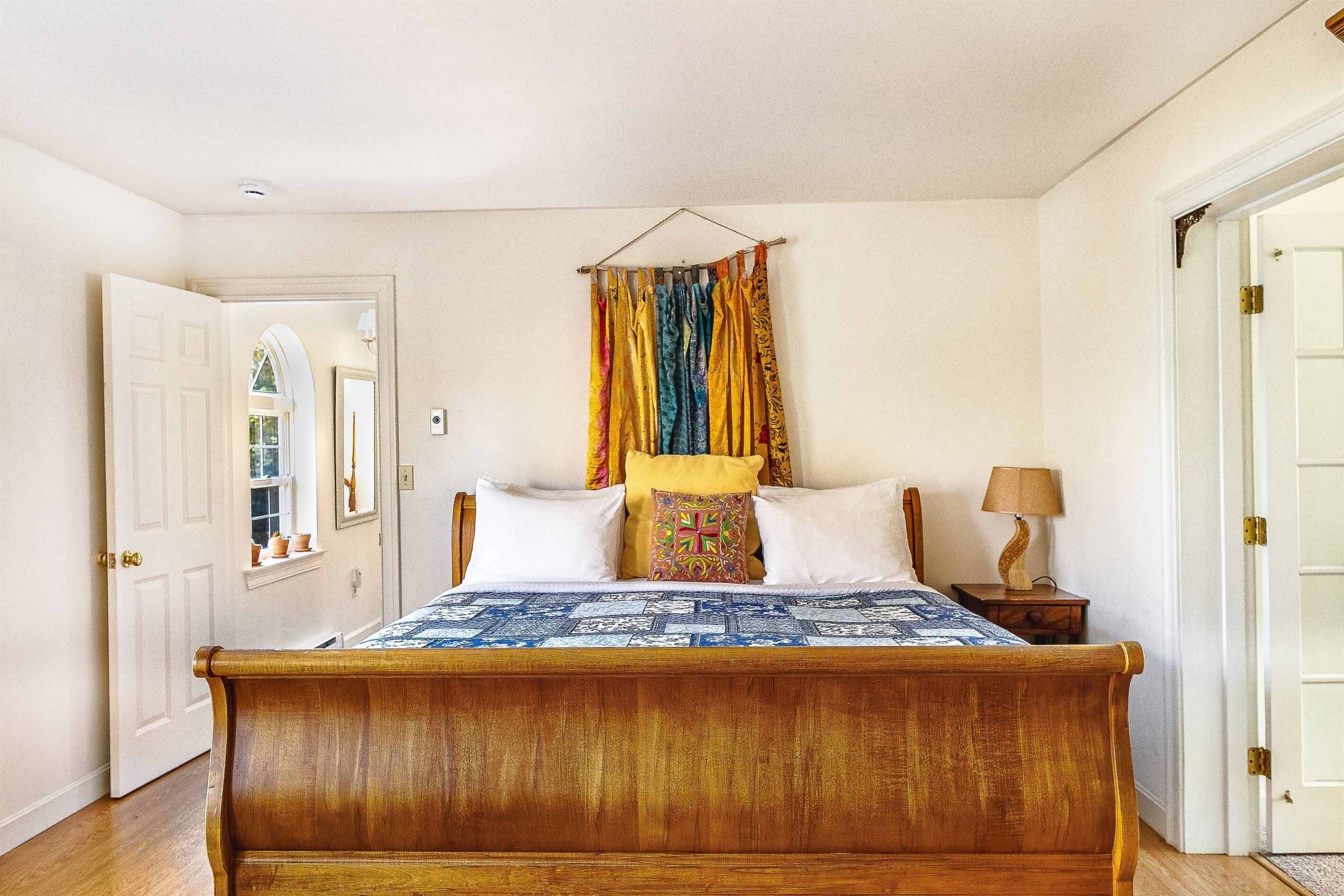 A bedroom with a wooden bed, a hanging curtain, a bedside table with a lamp, and a door.