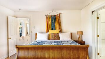 A bedroom with a wooden bed, a hanging curtain, a bedside table with a lamp, and a door.