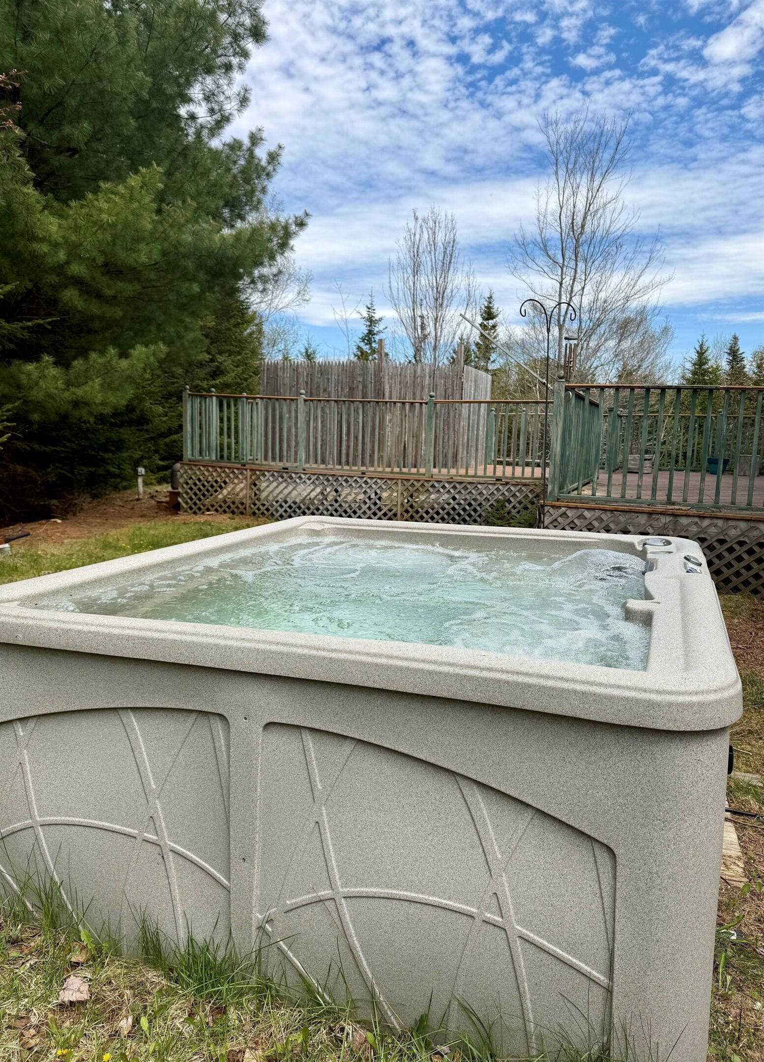 A hot tub in an outdoor setting with a wooden fence and trees in the background.