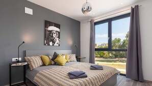 Un dormitorio moderno con una cama grande, una mesita de noche, una obra de arte en la pared y vistas amplias a través de un ventanal.