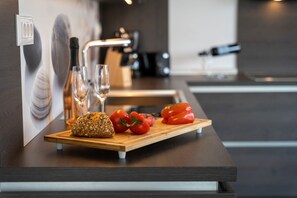 Eine moderne Küche mit einem Holztisch, auf dem Brot, Tomaten und eine Flasche liegen.