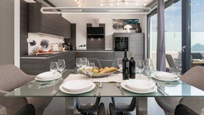 Un comedor moderno con una mesa de vidrio, platos blancos, copas de vino y un cuenco de frutas.