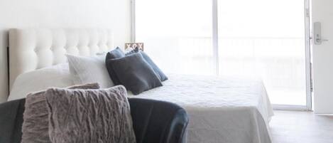 A bedroom with a large bed, a window, and a door.