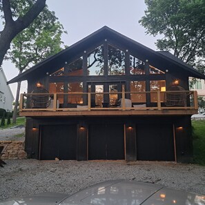 A two-story wooden cabin with a balcony, large windows, and a gravel driveway. - Luxury Lodge - 23 Min to Stadium - Sleeps 10 (Liberty)