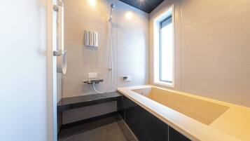 A modern bathroom with a bathtub, shower, and a window providing natural light.