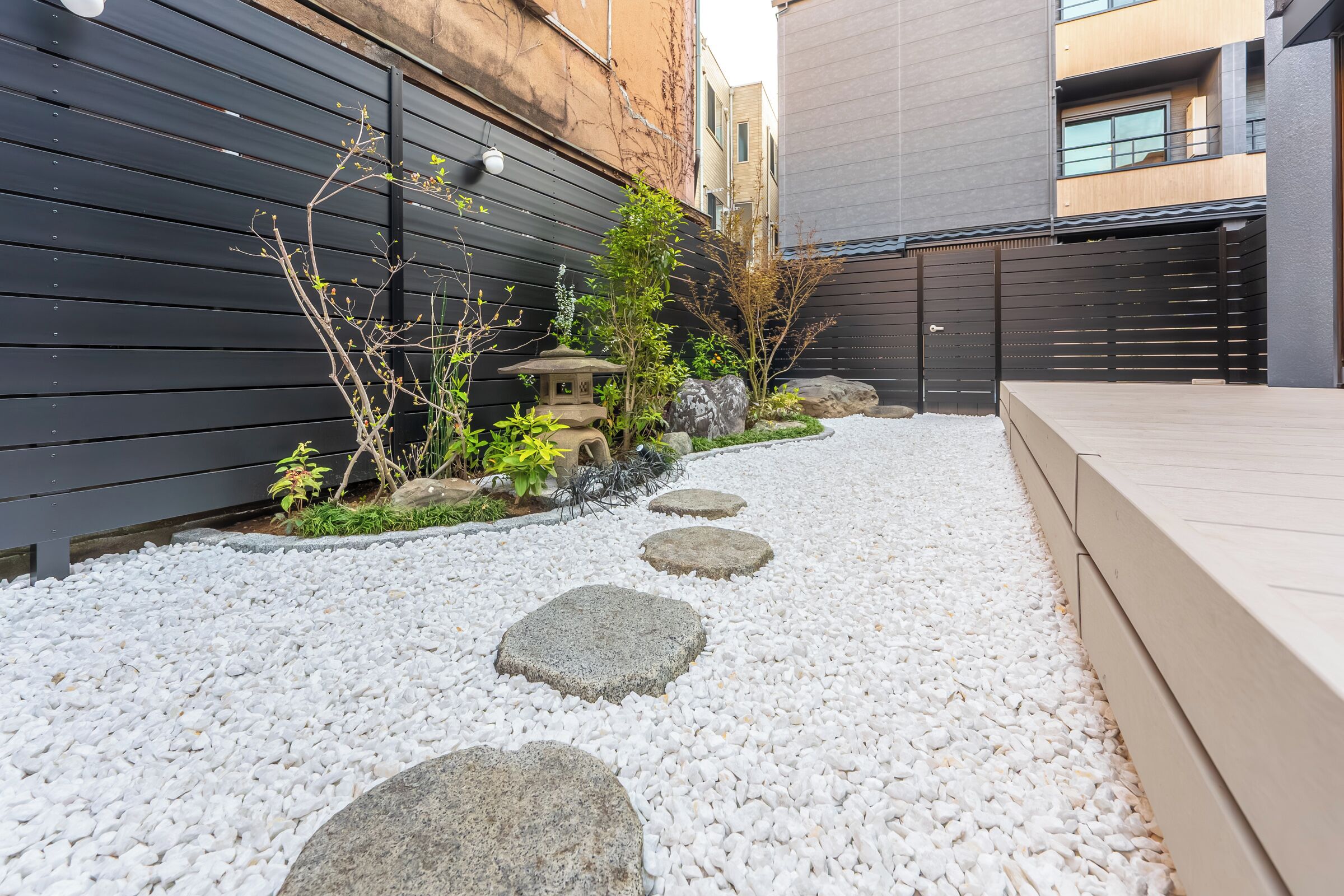 A garden with stepping stones, a small stone lantern, and a wooden fence.
