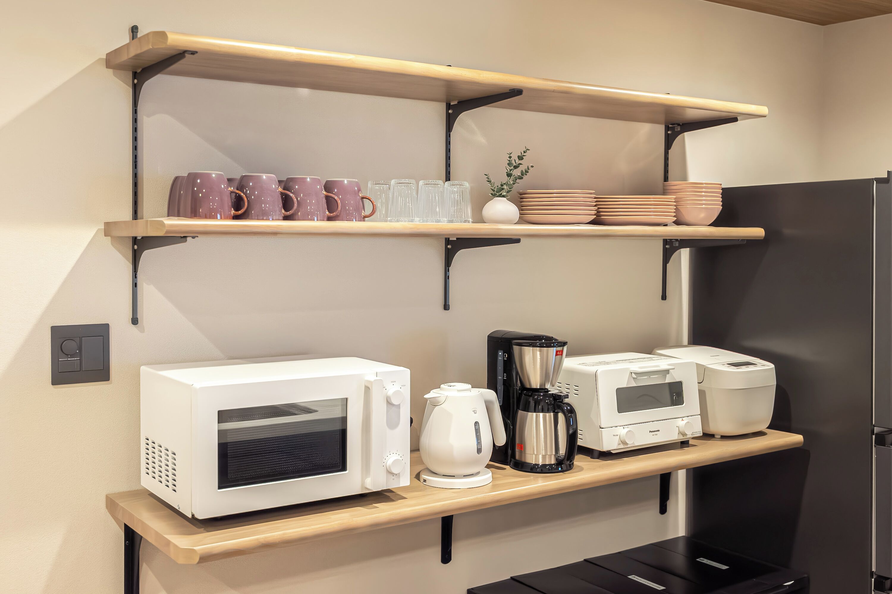 Une cuisine équipée d’un four à micro-ondes, d’une machine à café et d’un grille-pain, le tout posé sur une étagère en bois, avec un réfrigérateur en dessous.