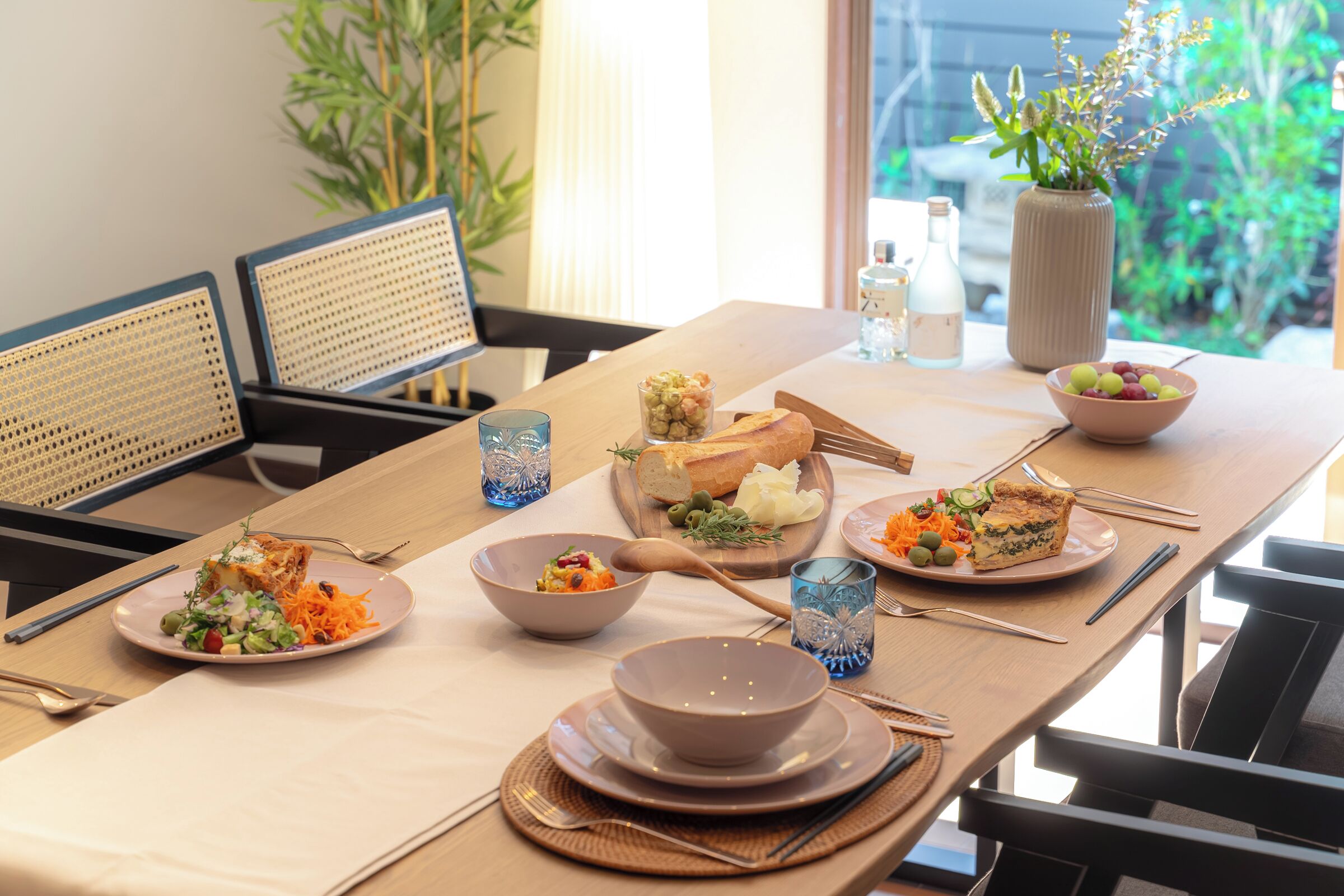 A dining table set with plates of food, a vase with flowers, and a window with a view of greenery.