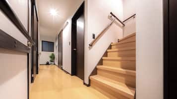 Un pasillo con una escalera de madera, una puerta y una planta en maceta.