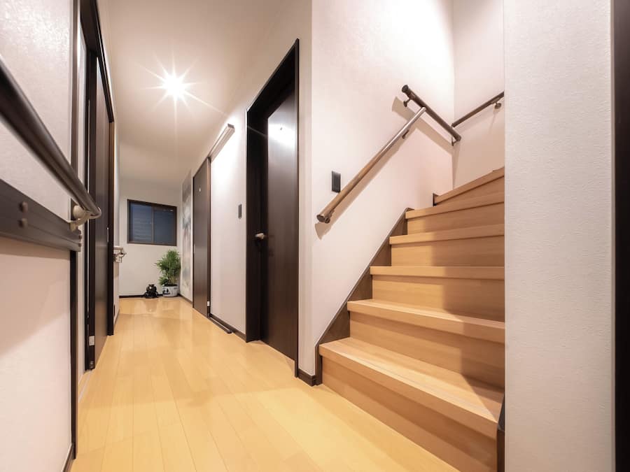 Un pasillo con una escalera de madera, una puerta y una planta en maceta.