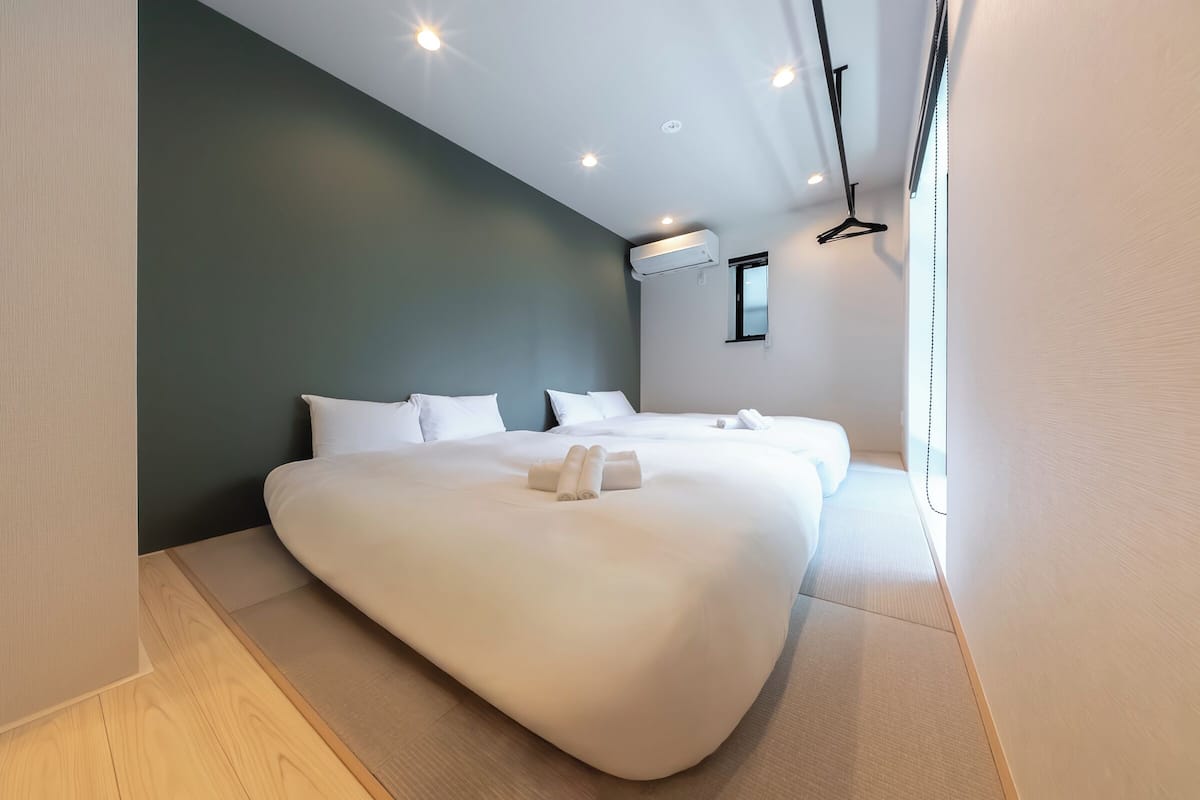 Una habitación de hotel moderna con una cama grande, una mesita de noche pequeña, aire acondicionado en la pared y una ventana con vistas.