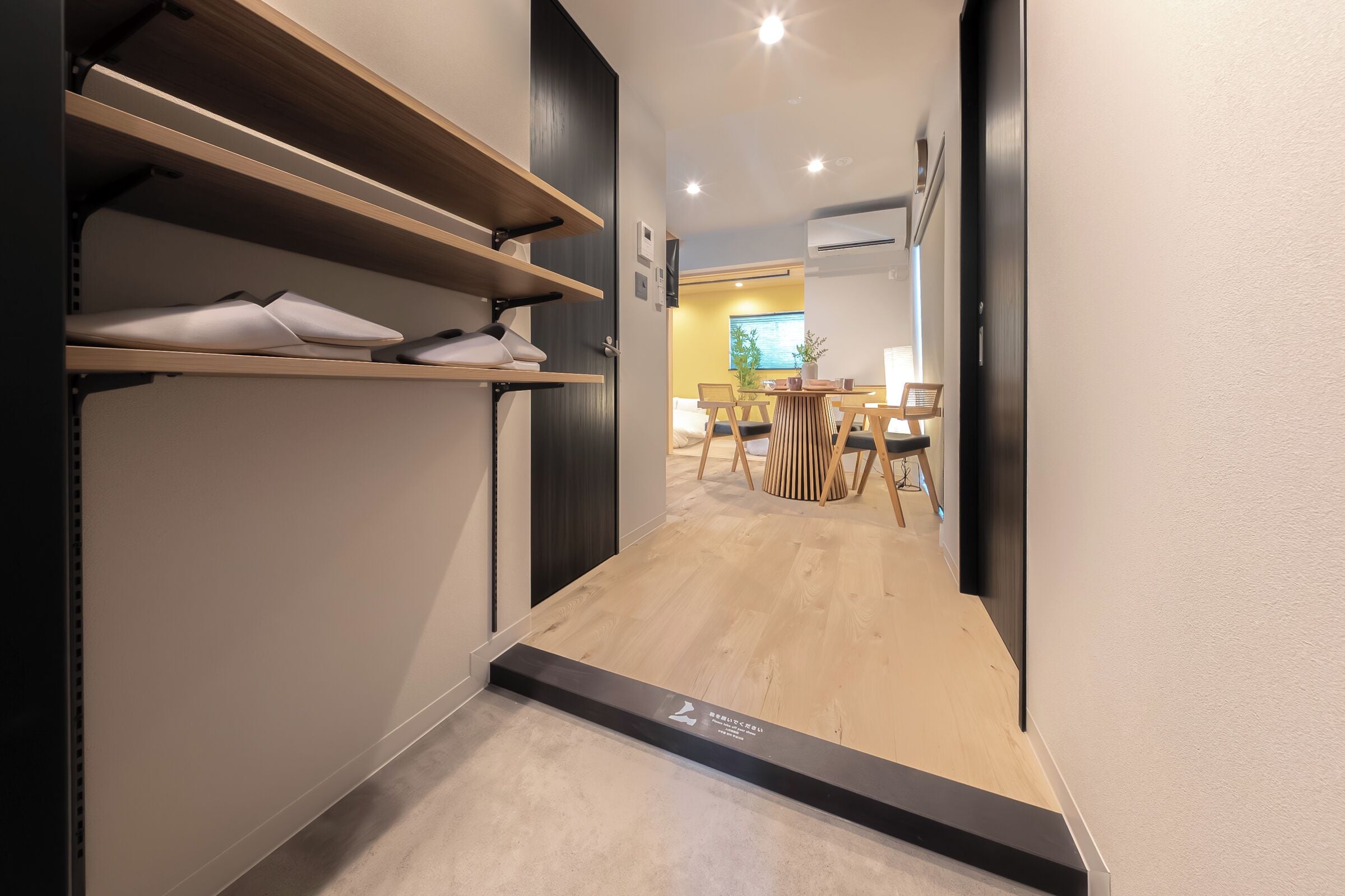 A hallway with wooden flooring, a shoe rack, and a dining area with chairs and a table.