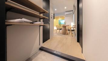 A hallway with wooden flooring, a shoe rack, and a dining area with chairs and a table.