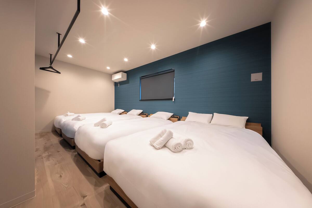 Habitación de hotel con tres camas, una lámpara en el techo, aire acondicionado montado en la pared y una ventana.