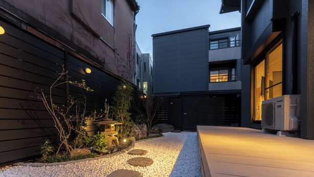 A pathway with stepping stones, a small garden with plants and rocks, and a building with a dark facade and windows. - Hotel Bokusyusou Tokyo (Tokyo)
