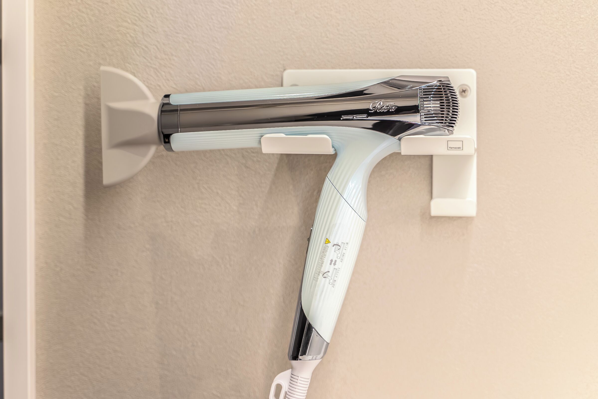 Un sèche-cheveux fixé au mur, doté d’un panneau de commande et d’un câble d’alimentation.