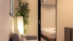 A modern hotel room with a bed, a chair, a large potted plant, and a wall-mounted light fixture. - Hotel Bokusyusou Tokyo (Tokyo)