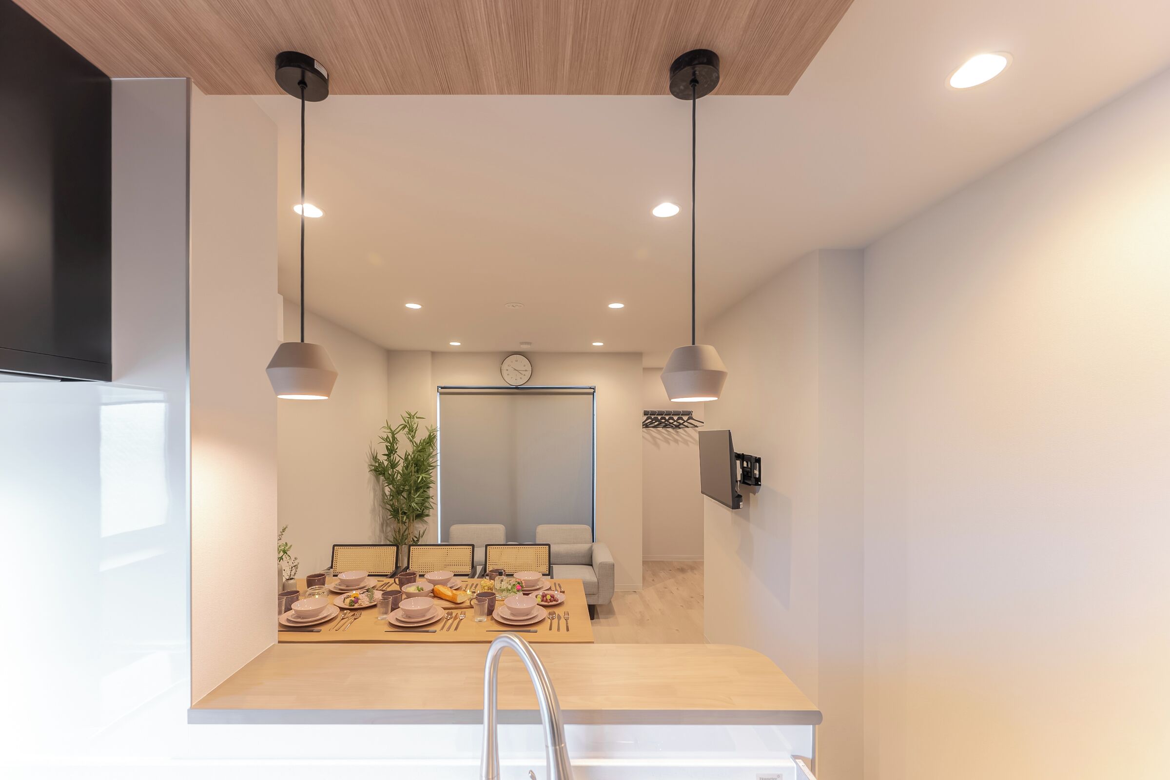 Un comedor moderno con una mesa de madera dispuesta para cuatro, un reloj en la pared e iluminación colgante.