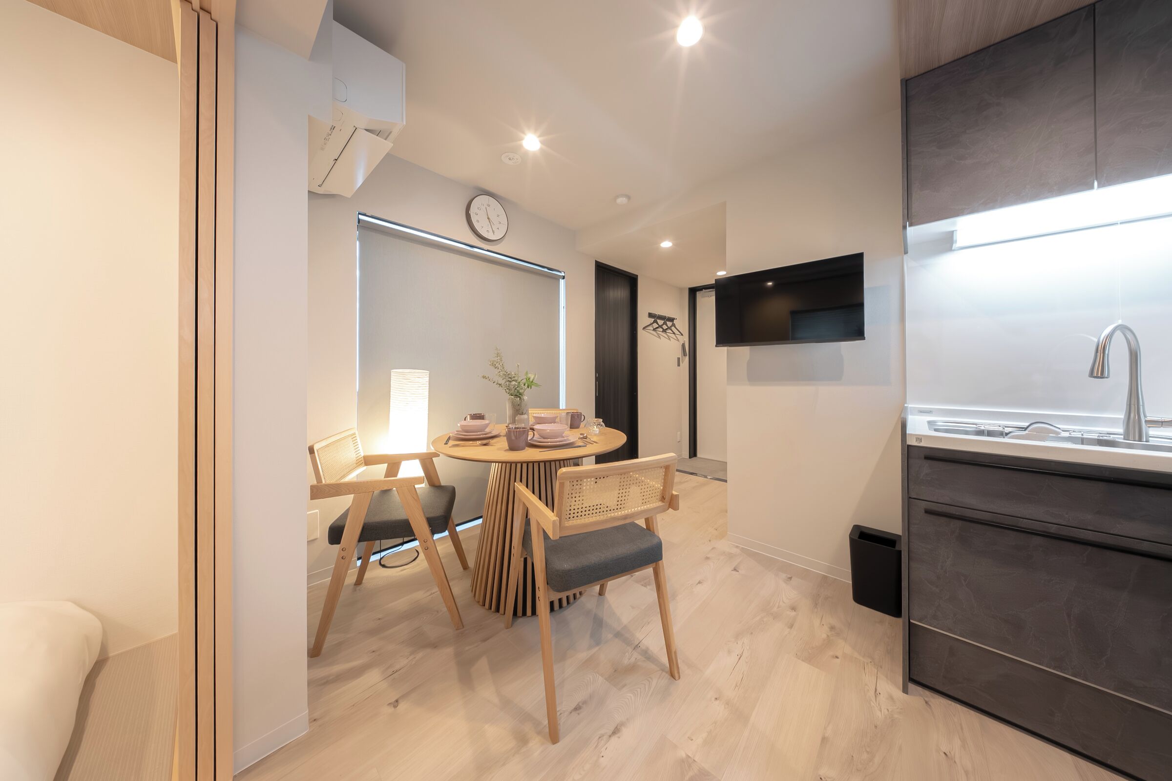 A modern kitchen with a built-in stove, a dining area with a round table and chairs, and a wall-mounted TV.