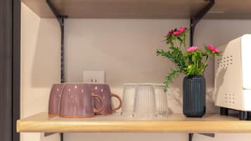 A shelf with ceramic mugs, clear glass tumblers, and a vase with flowers.