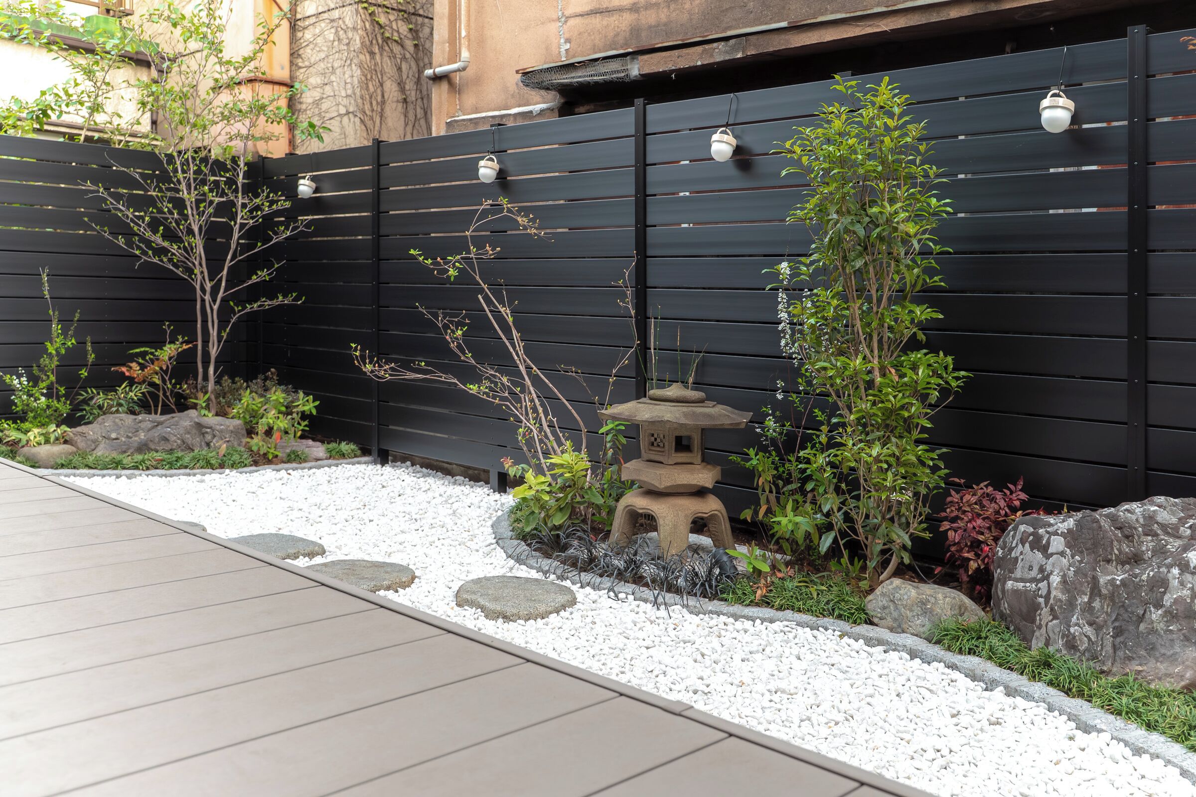 A garden with a black fence, white pebbles, rocks, and a small stone lantern.