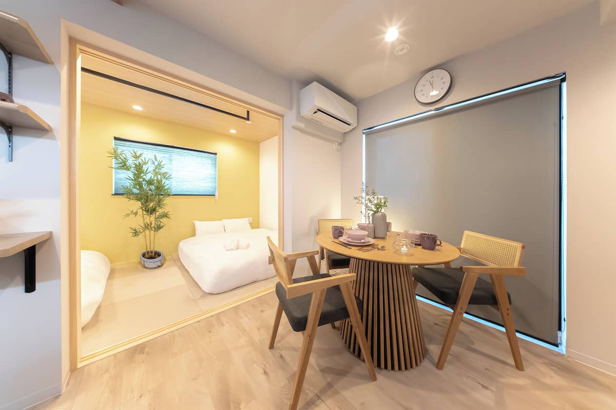 Una habitación moderna con una cama, una mesa de comedor con sillas, una planta en maceta y un reloj de pared.