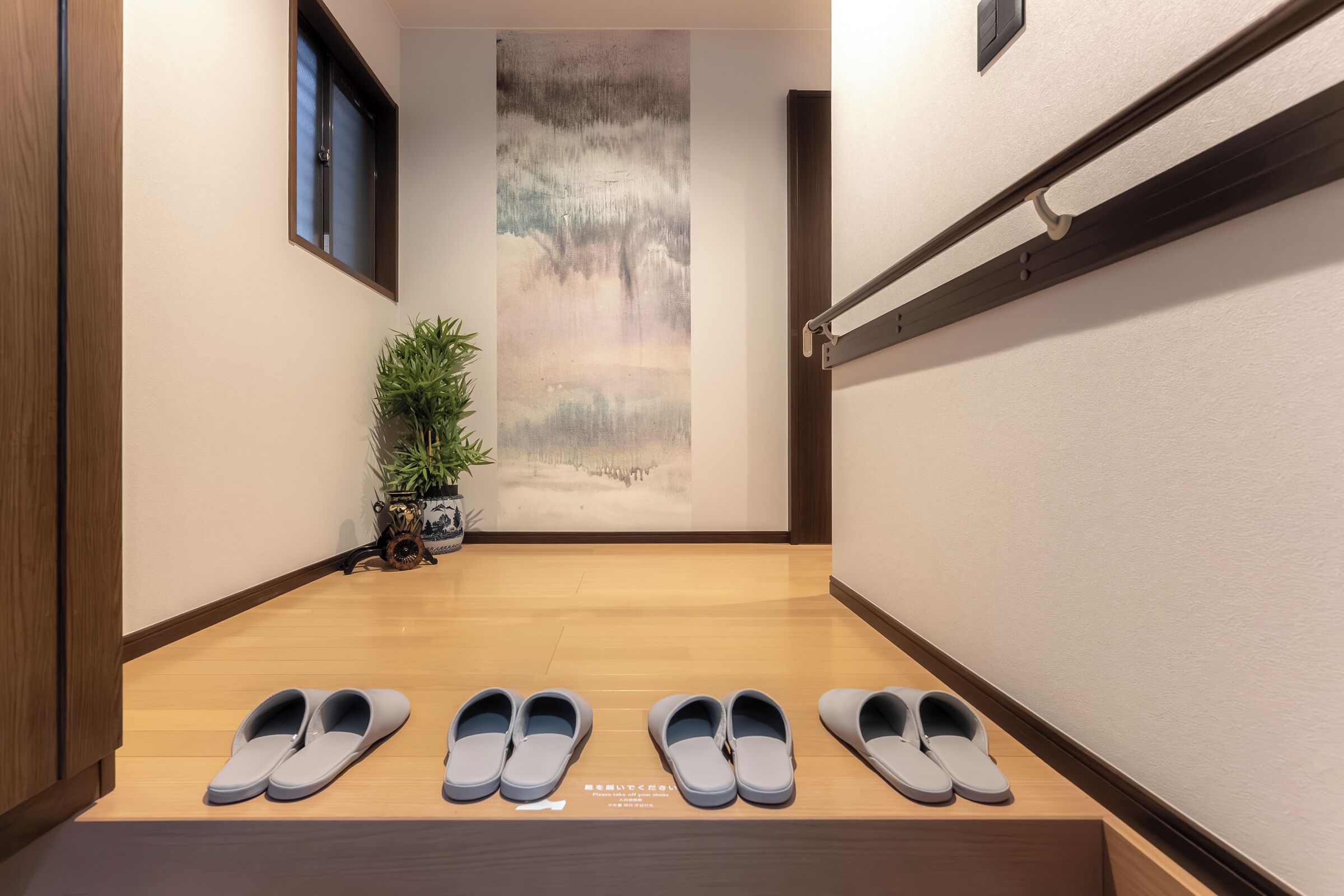 A hallway with a wooden floor, a wall-mounted rack, and a potted plant.